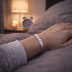 Hand liegt auf einer Bettdecke und trägt ein silbernes Magnetarmband am Handgelenk